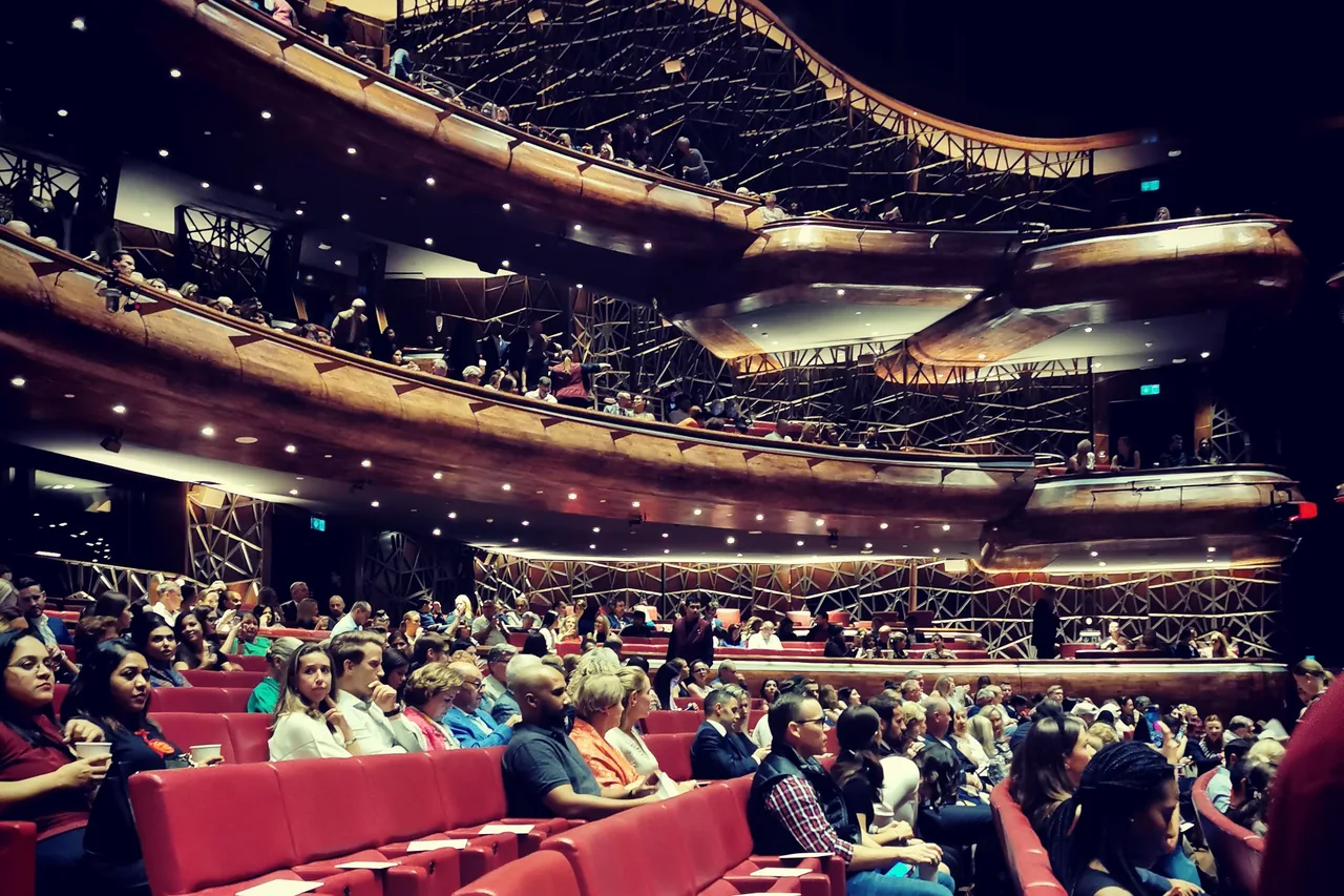 Audience taking their seats before one of the Dubai Opera 2026 shows, in the red-seated stalls and curved wooden balconies of the auditorium
